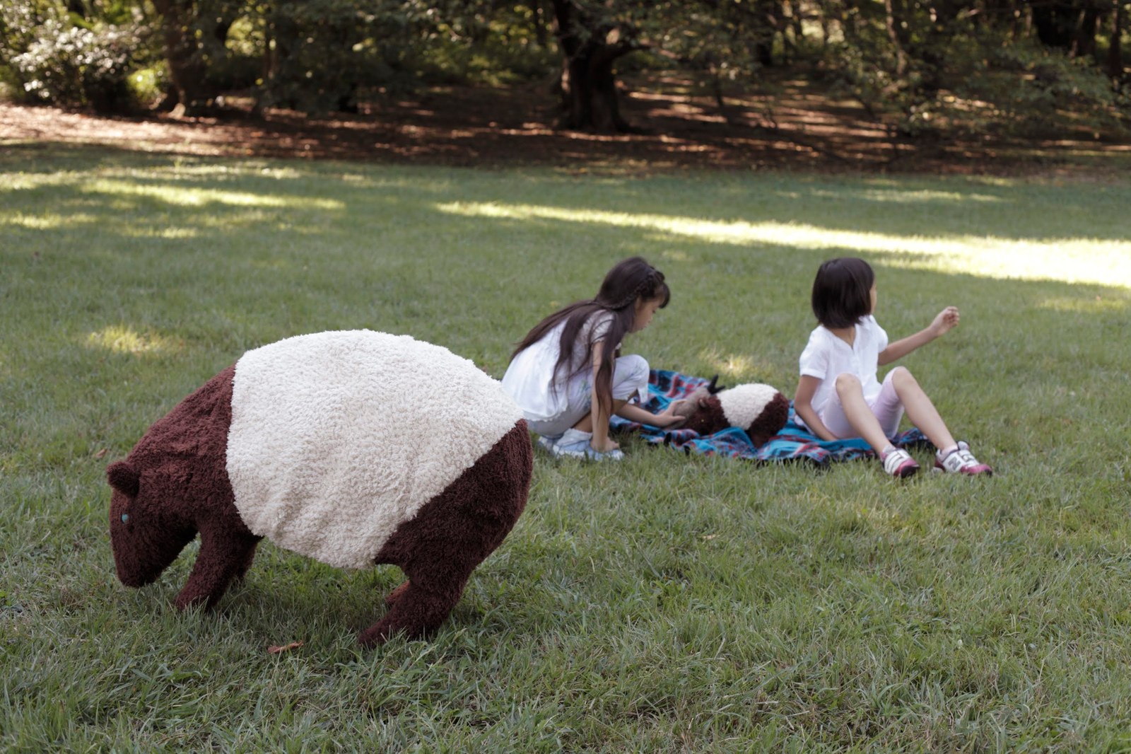 The tapir on the grass in a park, with children playing in the background