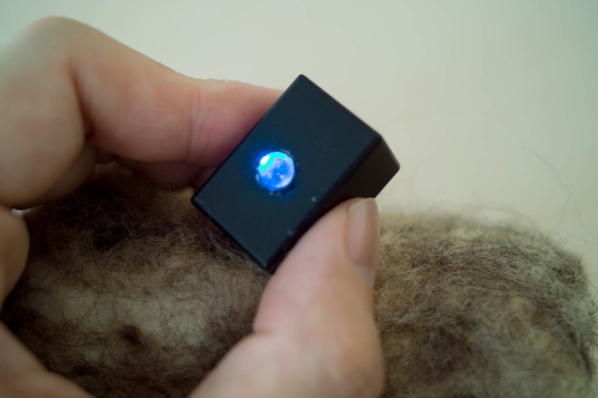 The Bokode module held between two fingers, its lens glowing blue